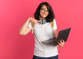 young-pleased-pretty-caucasian-schoolgirl-with-headphones-neck-wearing-glasses-back-bag-holds-points-laptop-pink-with-copy-space (1)